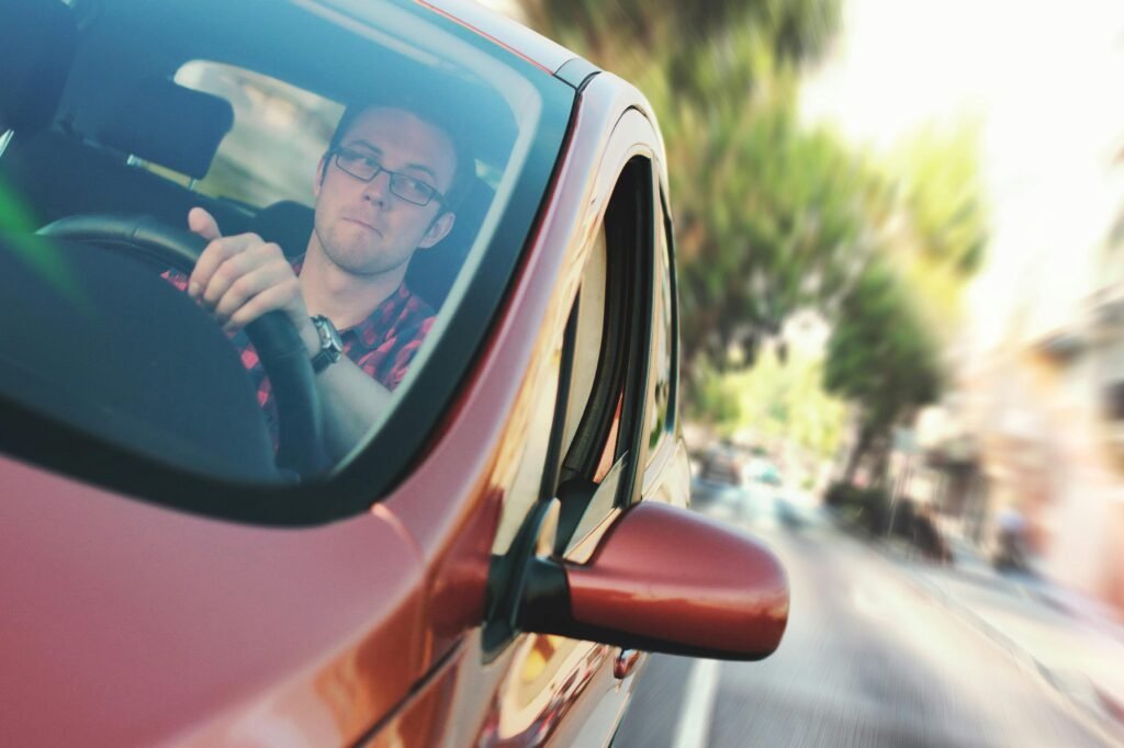 A man driving fast through a city street in a red car, showcasing motion and focus.
